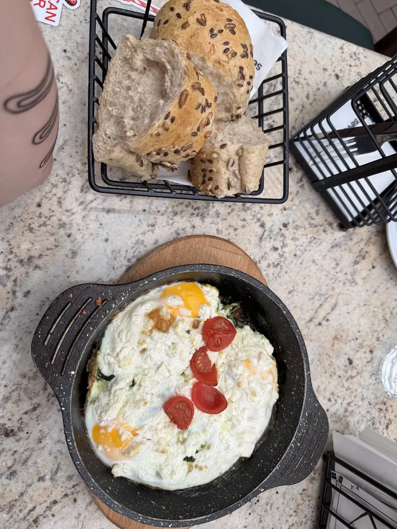 Eggs in a cast-iron pan with tomatoes, and a basket of bread