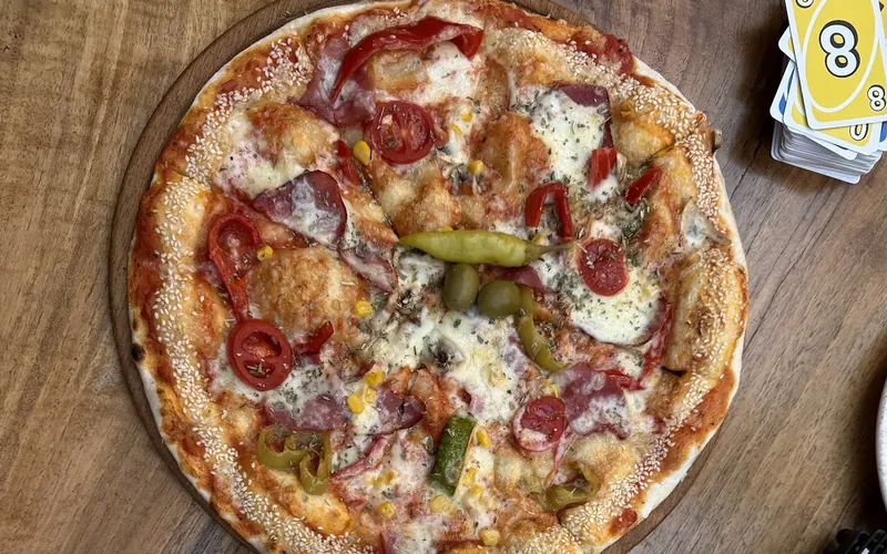 A pizza with sujuk, peppers and olives next to a rice dish
